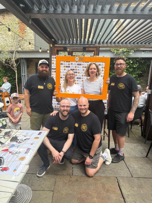A group posing with the orange FDS selfie frame in front of a sponsor board