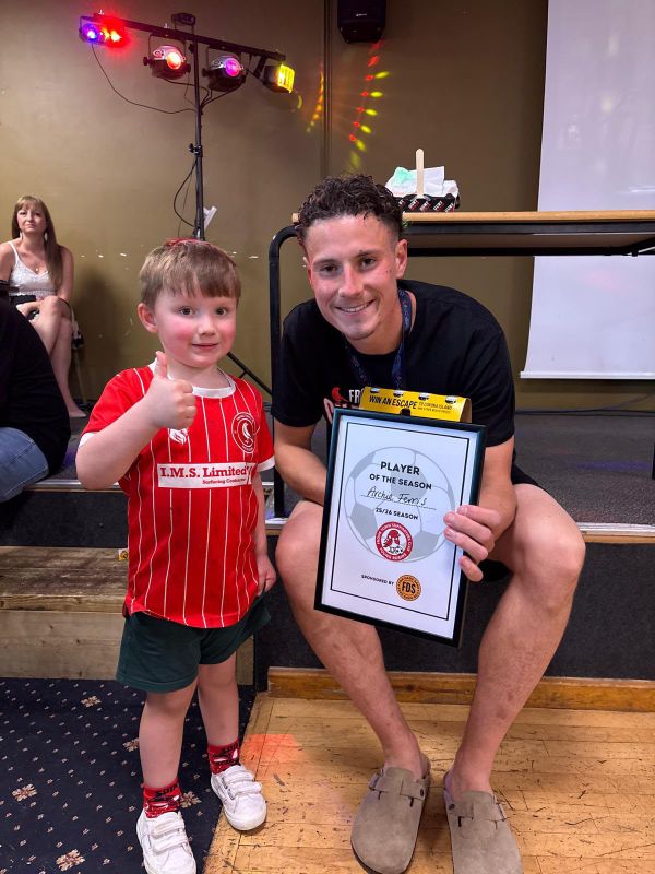 A young supporter giving a thumbs up beside a Player of the Season certificate sponsored by FDS