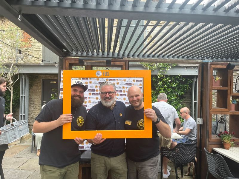 Three men holding the orange FDS selfie frame in a pub garden